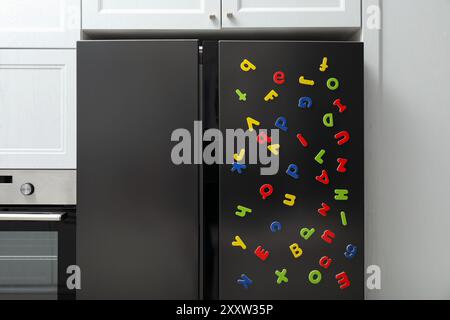 Viele helle magnetische Buchstaben auf dem Kühlschrank in Innenräumen. Alphabet lernen Stockfoto