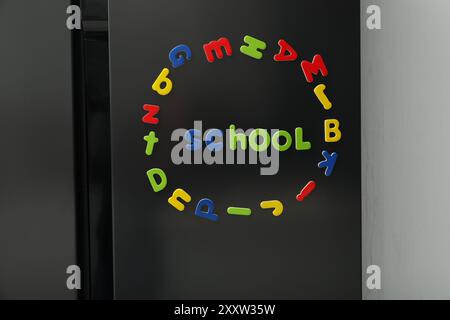 Wortschule und Kreis aus vielen hellen magnetischen Buchstaben auf dem Kühlschrank drinnen. Alphabet lernen Stockfoto