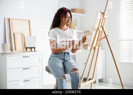 Schöne Frau, die im Studio ein Bild auf Leinwand zeichnet Stockfoto