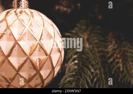 Nahaufnahme einer weißen Weihnachtskugel mit goldenem Glitzer, die an einer Tanne hängt. Festliches Konzept mit Kopierraum. Stockfoto