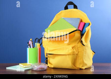 Rucksack mit anderem Schulpapier auf Holztisch vor blauem Hintergrund Stockfoto