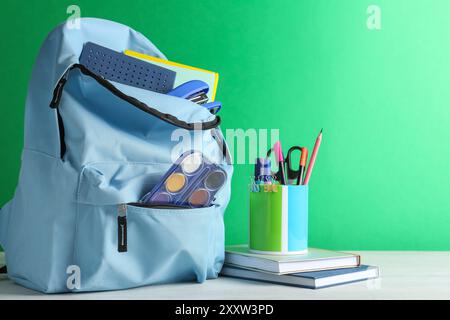 Rucksack mit anderem Schulpapier auf weißem Tisch vor grünem Hintergrund Stockfoto