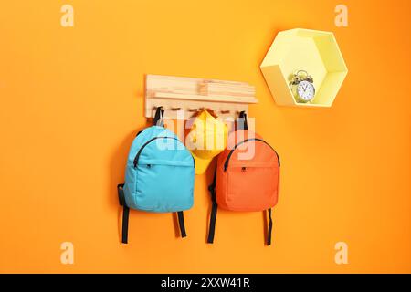 Helle Rucksäcke, Kappe und Wecker an orangefarbener Wand Stockfoto