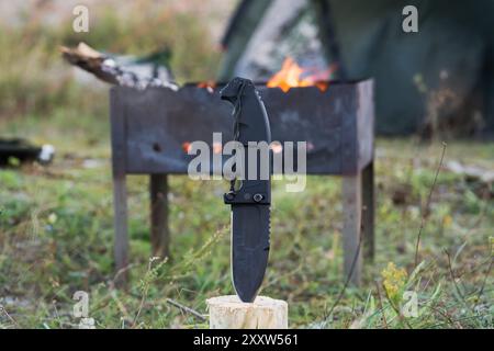 Camping in der Natur mit einem Grill, einem Klappmesser zum Holzhacken und einem brennenden Grill. Stockfoto