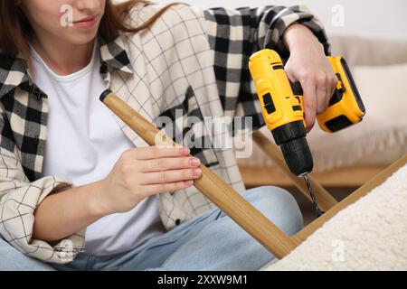 Frau mit elektrischem Schraubenzieher, der den Sessel im Zimmer zusammenstellt, Nahaufnahme Stockfoto