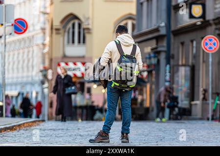 Riga, Lettland - 6. November 2020: Ein junger Mann hält auf einer kopfsteingepflasterten Straße inne, während andere in der Nähe spazieren. Stockfoto