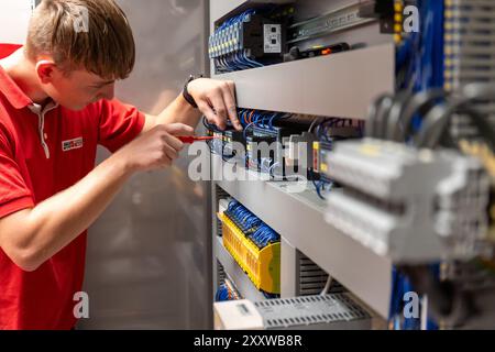 Ranstadt, Deutschland. August 2024. Felix Hensel, ausgebildeter Mechatroniker, verdrahtet den Hauptschaltschrank einer FFS-Maschine (Form-Fill-Seal) bei der Hassia Verpackungsmaschinen GmbH. Der Maschinenbauspezialist baut Umformmaschinen, Abfüllmaschinen und Dichtmaschinen und sucht nach neuen Talenten. Quelle: Christian Lademann/dpa/Alamy Live News Stockfoto