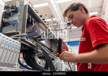 Ranstadt, Deutschland. August 2024. Elias Pohl, ausgebildeter Elektroniker, verdrahtet einen kleinen Maschinensteuerschrank an einer FFS-Maschine (Form-Fill-Seal) bei der Hassia Verpackungsmaschinen GmbH. Der Maschinenbauspezialist baut Umformmaschinen, Füll- und Dichtmaschinen und sucht Nachwuchstalente. Quelle: Christian Lademann/dpa/Alamy Live News Stockfoto