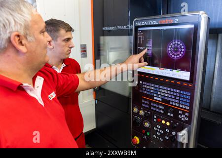 Ranstadt, Deutschland. August 2024. Instruktor Christian Seum (l), ebenfalls Teamleiter Produktion, gibt Jonathan Seum, Auszubildender Industriemechaniker, eine Einführung in ein modernes CNC-Dreh-/Fräszentrum bei der Hassia Verpackungsmaschinen GmbH. Der Maschinenbauspezialist baut Umformmaschinen, Füll- und Dichtmaschinen und sucht Nachwuchstalente. Quelle: Christian Lademann/dpa/Alamy Live News Stockfoto