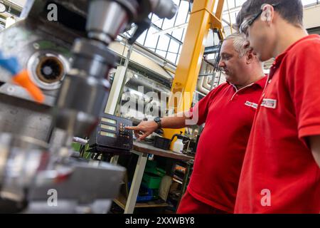 Ranstadt, Deutschland. August 2024. Jonas helle (r), ausgebildeter Bediener von Schneidemaschinen, erhält bei der Hassia Verpackungsmaschinen GmbH von Trainer Christian Seum, ebenfalls Teamleiter Produktion, Einweisung in eine konventionelle Fräsmaschine. Der Maschinenbauspezialist baut Umformmaschinen, Füll- und Dichtmaschinen und sucht Nachwuchstalente. Quelle: Christian Lademann/dpa/Alamy Live News Stockfoto