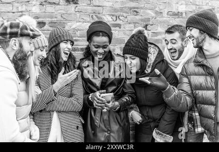 Eine Gruppe von Freunden lacht und genießt einen lustigen Moment zusammen, während sie ein Smartphone anschauen, das in einer offenen Schwarzweißaufnahme aufgenommen wurde. Stockfoto