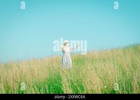 Glückliche reife Frau mit Wildblumen auf einem hohen Grasfeld an einem hellen Sommertag. Stockfoto