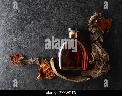 Flasche Brandy und alte Schlangen mit getrockneten Weinblättern auf schwarzem Steinhintergrund. Draufsicht. Stockfoto