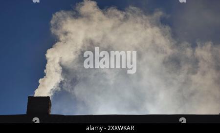 Die Silhouette aus Rauch vor der Sonne aus dem Schornstein eines Dorfhauses. Stockfoto