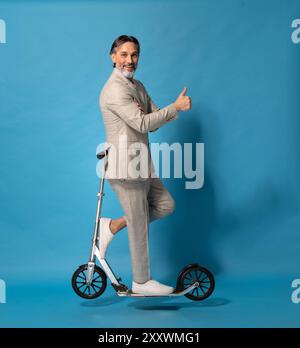 Ein Mann im Anzug steht auf einem Roller. Er gibt einen Daumen hoch. Die Szene ist positiv und lustig Stockfoto