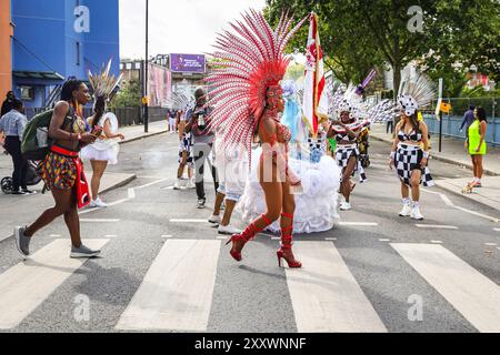 London, UK, 26. August 2024. Tänzer überqueren die Straße in Kostümen. Die Teilnehmer der Paraiso School of Samba, einer der größten Gruppen mit fast 200 Künstlern und Musikern, kommen vom frühen Morgen bis zum Beginn der Prozession um 12 Uhr. Am Montag findet der Karnevalszug von MAS-Bands, Schlagzeugern und karibischen und südamerikanischen Salsa-, Samba- und Soca-Gruppen statt. Am zweiten von zwei Tagen des Karnevalsfestes in Notting Hill feiern die Nachtschwärmer das Wochenende der Bank Holiday, an den Soundsystemen, an den Ständen und an den Veranstaltungsorten entlang der Karnevalsroute. Stockfoto