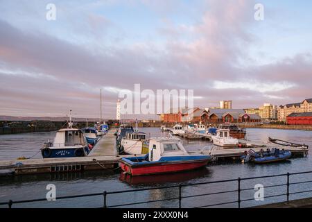 EDINBURGH - 13. JANUAR 2024: Der malerische Sonnenuntergang wirft warmes Licht über den Leuchtturm und die Boote legen am Pier im Hafen von Newhaven an. Stockfoto