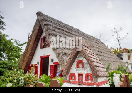 Ein einst typisches dreieckiges Haus in Santana, Madeira mit einem Strohdach, das am 5. August 2024 hinter einer Modellversion im Garten gesehen wurde. Stockfoto
