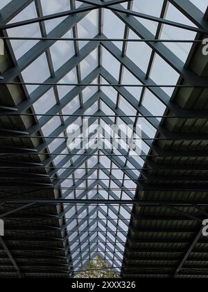 Unter dem verglasten Dach: Metallkonstruktionsmuster in Licht und Schatten. Blaue Decke. Stockfoto