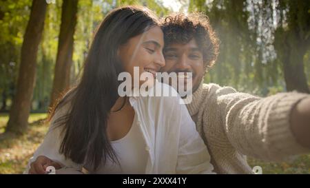 Sorgloses multirassisches Paar arabisch indischer männlicher Freund glückliche hispanische Freundin Frau macht Foto auf Handy-Gerät draußen im Park Mann Stockfoto