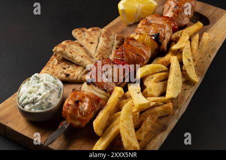 Nahansicht des vom Schwein marinierten Souvlaki mit gebratenen Kartoffeln, Pita und Joghurt Dip auf Holzbrett. Stockfoto