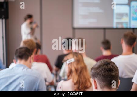 Das Publikum hört dem Sprecher während eines informativen Vortrags in Konferenzräumen aufmerksam zu. Verschwommener Lautsprecher im Hintergrund sorgt für mehr Aufmerksamkeit auf die Teilnehmer. Stockfoto