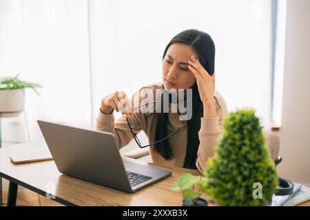 Müde Junge asiatische koreanische Arbeiterstudentin kurze Pause in der Online-Arbeit Brille entfernen Massage weibliche Angestellte überarbeitet durch Laptop Stockfoto