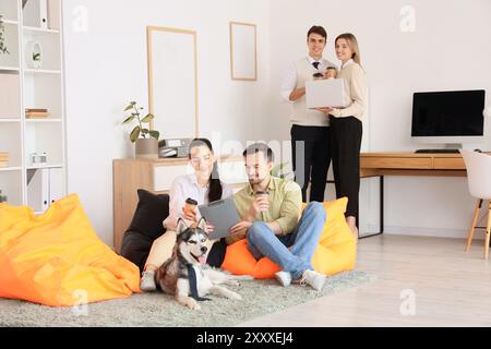 Junge Leute mit Kaffee und lustigem Husky-Hund im Büro Stockfoto