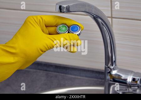 Klempnerhand in gelben Gummihandschuhen mit neuem und altem verstopftem Wasserhahnbelüfter Stockfoto