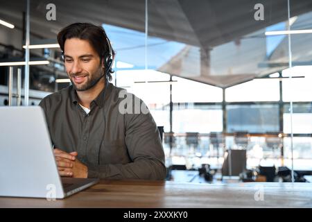 Glücklicher junger Mann ruft den Contact Center-Mitarbeiter an, der im Büro auf einem Laptop arbeitet. Stockfoto