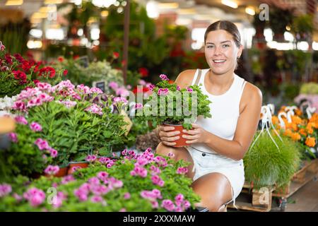 Junge Mädchen, die Geranie im Blumentopf auf dem Pflanzenmarkt hält Stockfoto