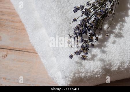 Lavendelblumen neben weißem Baumwollhandtuch auf hölzernem Hintergrund. Aromatherapie und organisches Konzept. Stillleben getrockneter Lavendelkräuter. Ökologisches nachhaltiges Konzept Stockfoto