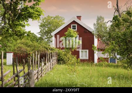 Typisches rotes Holzhaus im ländlichen Schweden, mit traditionellem Zaun, Wiesen und Obstbäumen. Perfektes Klischee für das Bild Schwedens in der Welt Stockfoto