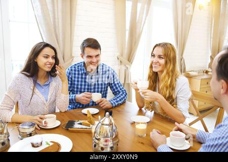 Gruppe von vier glückliche Freunde treffen und reden und Essen von Nachtischen auf einem Tisch zu Hause Stockfoto