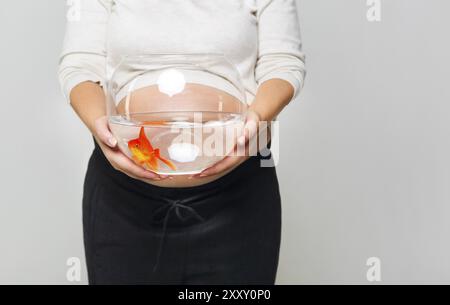 Glücklich schwanger Frau ein Goldfischglas mit einem Goldfisch in ihren Händen hält. Pflege und Liebe Konzept Stockfoto