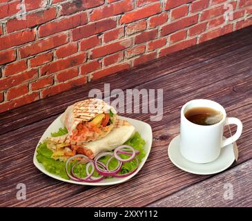 Eine Tasse schwarzen Tee in Beutel und ein Teller mit gehacktem Fleisch Shawarma auf einem Salatblatt mit Zwiebelringen auf einem dunklen Holztisch. Nahaufnahme. Stockfoto