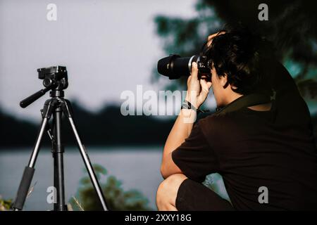 Junger Mann, der am Ufer des Sees eine Kamera aufstellt. Rückansicht der Kamera mit Stativ für männliche Einstellungen Stockfoto