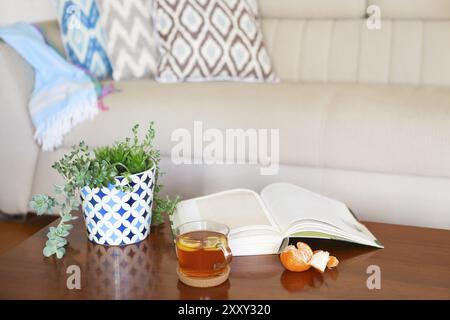 Topf mit Sukkulenten und aufgeschlagenes Buch mit dem Tee auf Holztisch. Gemütliche Zimmer Stockfoto