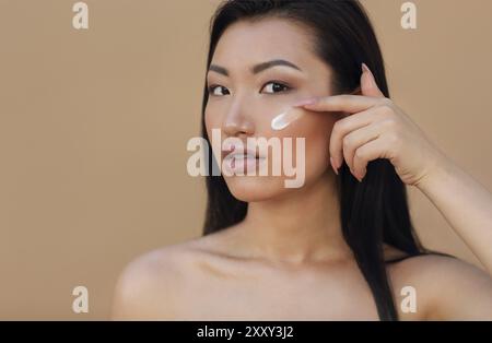 Junge schöne asiatische Frau Anwendung creme, beige Hintergrund isoliert Stockfoto
