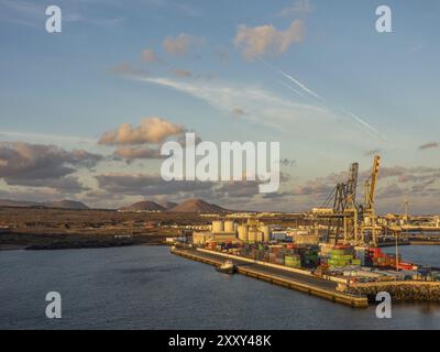Industriehafen mit Containern und Kränen am Ufer, Berge und Industriebauten im Hintergrund bei Sonnenuntergang, lanzarote, Kanarische Inseln Stockfoto