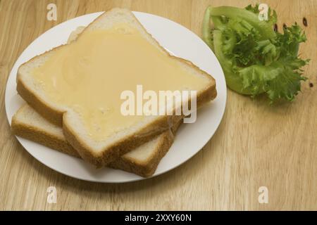 Brot und gezuckerte Kondensmilch in einem weißen Teller auf einem Holzbrett Stockfoto