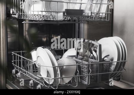Vorderansicht der offenen automatischen Edelstahl-Einbaumaschine mit vollständig integrierter Steuerung der oberen Spülmaschine mit sauberen Utensilien, Besteck, Gläsern und DIS Stockfoto