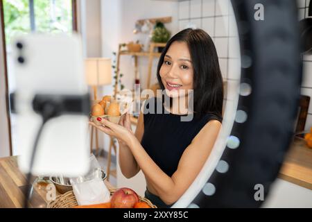 Eine attraktive asiatische Food-Bloggerin oder Content-Creatorin kocht vor der Kamera, spricht und zeigt ihre Zutaten für ein spezielles Menü Stockfoto