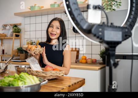 Eine attraktive asiatische Food-Bloggerin oder Content-Creatorin kocht vor der Kamera, spricht und zeigt ihre Zutaten für ein spezielles Menü Stockfoto