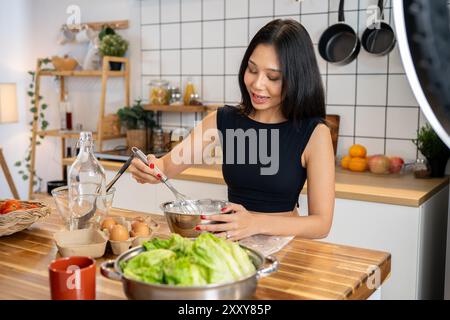Eine attraktive asiatische Food Bloggerin kocht vor der Kamera und erklärt das Rezept, während sie ein Video aufnimmt, in dem sie gesundes Foo macht Stockfoto