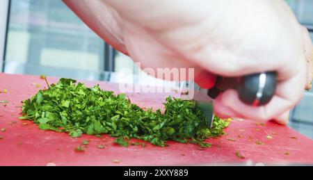 Männlichen Chef schneiden Petersilie mit großen Messer auf Schneidebrett rot Stockfoto