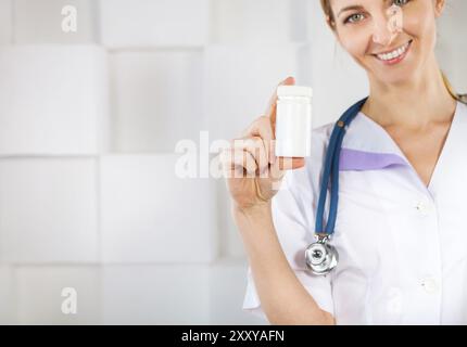 Ziemlich lächelnde Frau Doktor in uniform zeigt ein Medizinfläschchen und Blick in die Kamera Stockfoto