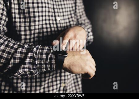 Mann in lässiger Kleidung klickt Handuhren, Armband, schwarzer verschwommener Hintergrund. Stockfoto