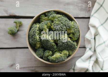 Grüner frischer Brokkoli in Schüssel auf hölzernem Hintergrund, weißes Handtuch. Konzept für gesunde Ernährung. Stockfoto