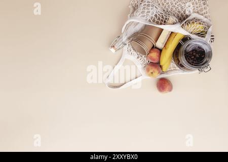 Umweltfreundliche Sommer konzeptionelle Wohnung lag auf beigem Hintergrund mit Öko Einkaufstasche, Küche Recycling Besteck, Glasflasche, Bananen und Pfirsich, Papier c Stockfoto